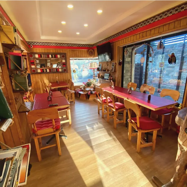 Cafetería del hostal con mesas rojas, sillas de madera y repisas con libros