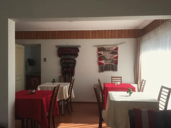 Comedor con manteles rojos y blancos junto a telares en la pared