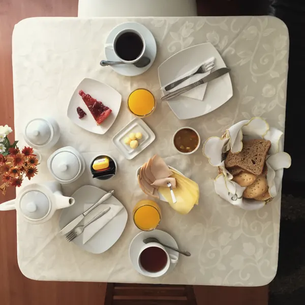 Mesa de desayuno vista desde arriba con café, té, jugo de naranja, pan, jamón y queso