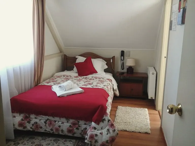 Habitación single con cubrecama rojo y velador